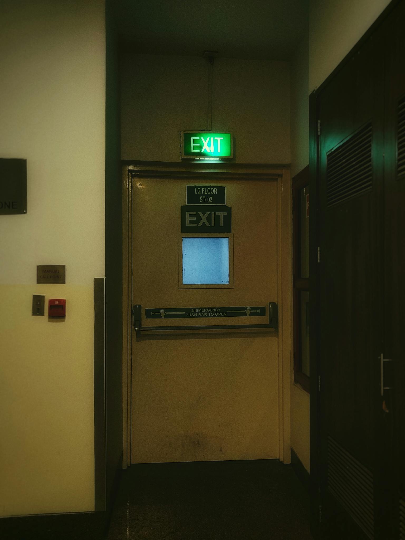 A dimly lit emergency exit door in a corridor with signage and safety indications.