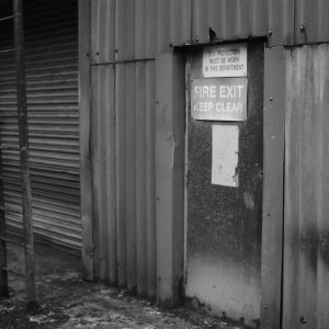 Black and white image of a rusty fire exit in an abandoned industrial building.