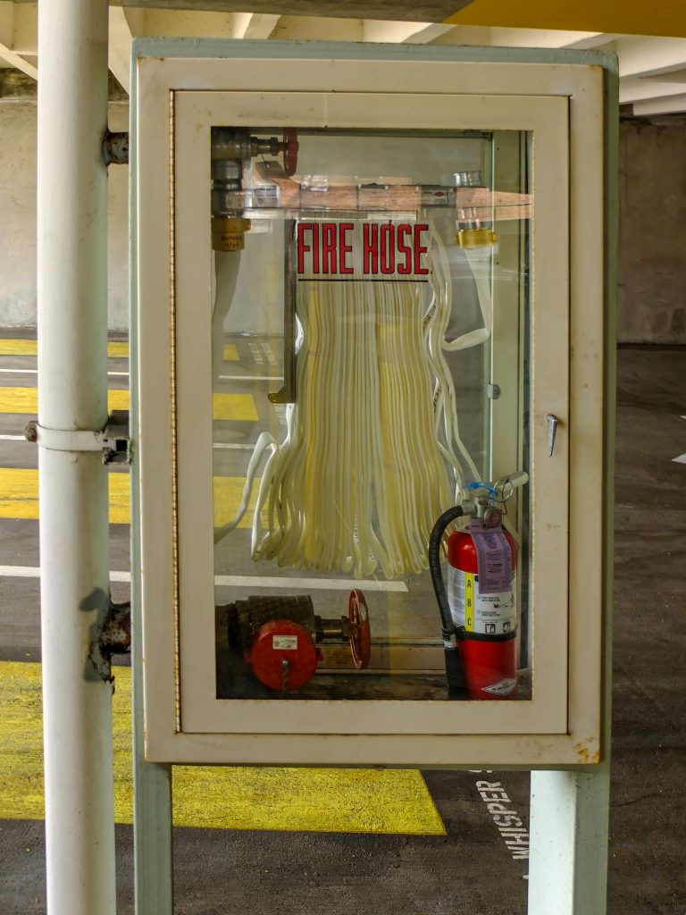Vertical shot of a fire hose and extinguisher in a parking garage, ensuring safety.